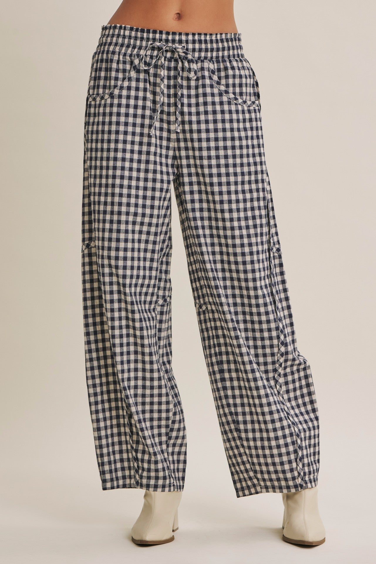 Black and white gingham wide-leg pants with a drawstring waist, modeled with off-white ankle boots against a solid beige background.