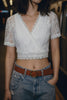 Person wearing a white lace top and blue jeans with a brown belt.