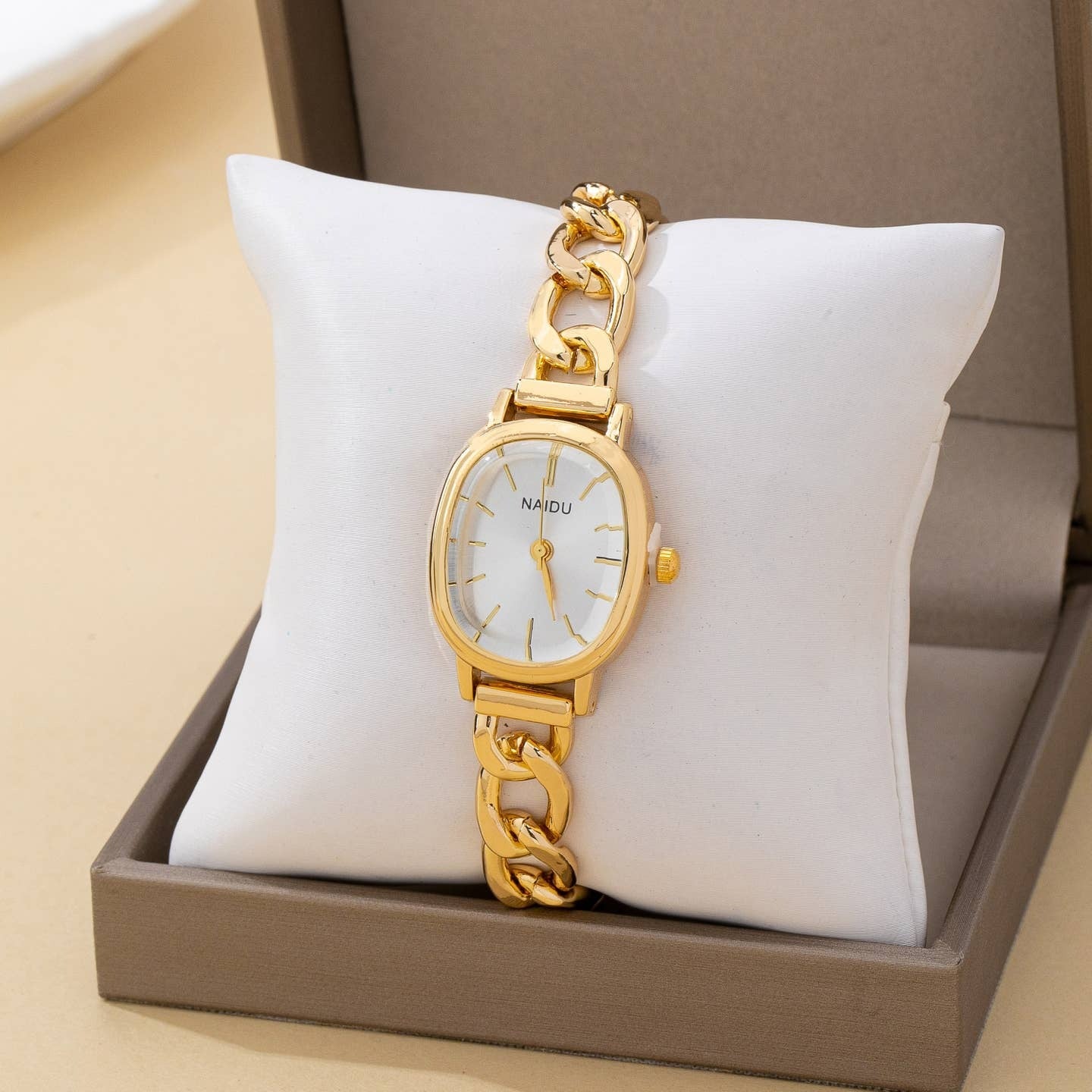 Gold wristwatch with chain design on a white cushion in a brown box