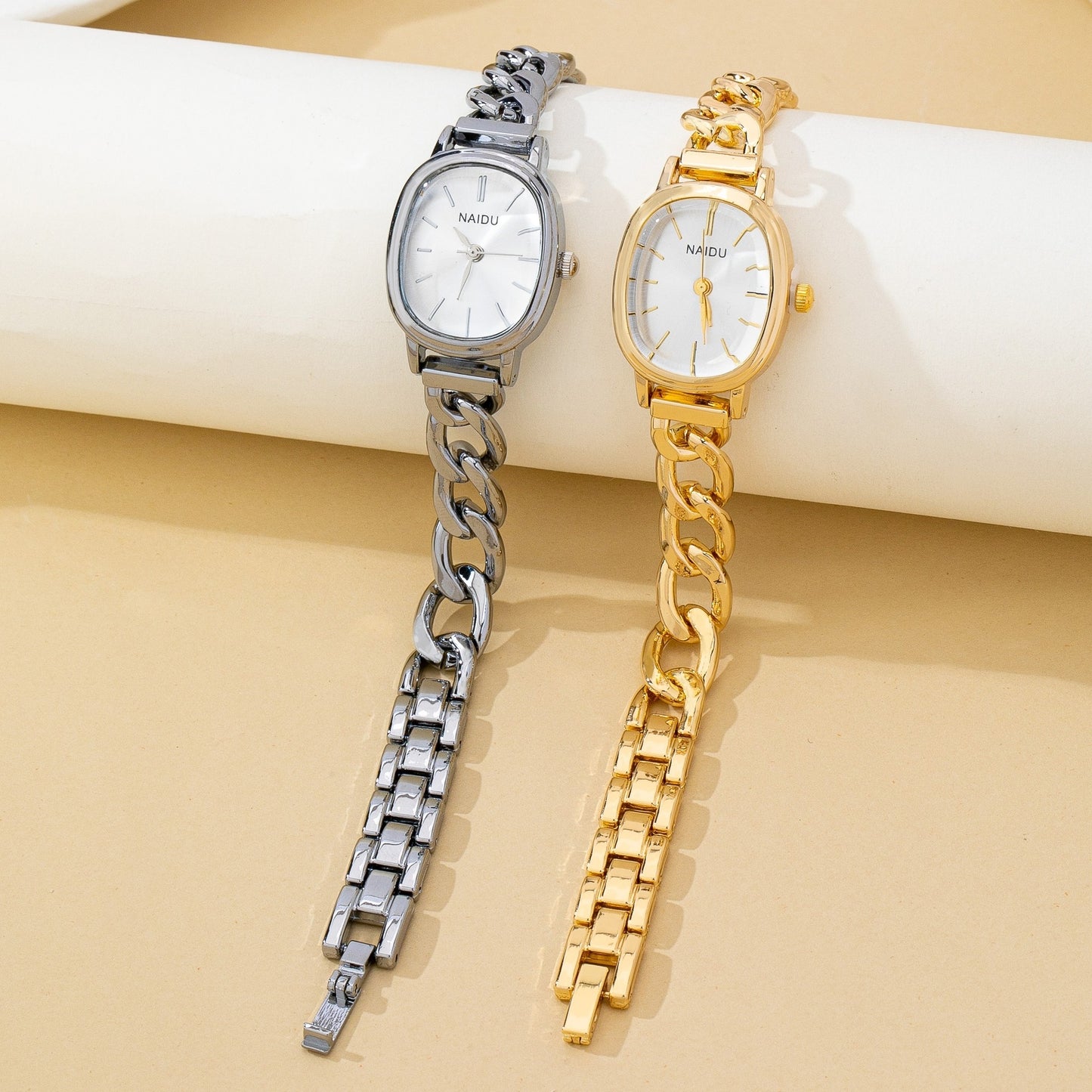 Two women's analog wristwatches with chunky chain straps, one in silver-tone metal and one in gold-tone metal, displayed on a beige surface with a white cylindrical prop. The brand name 'MAOU' is visible on the white dials.