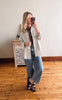 Woman taking a mirror selfie wearing a light-colored jacket and blue jeans in a room with wooden flooring.