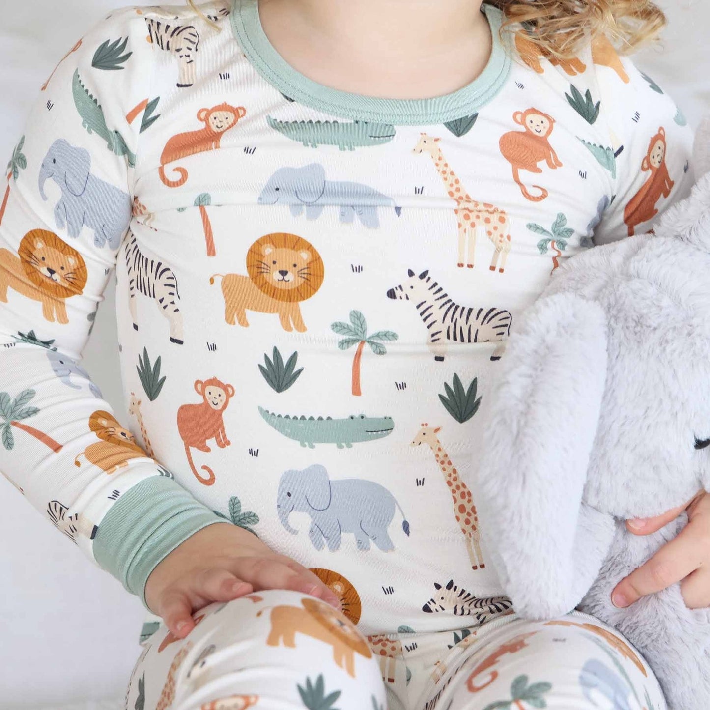 Child wearing pajamas with animal pattern sitting on a white blanket