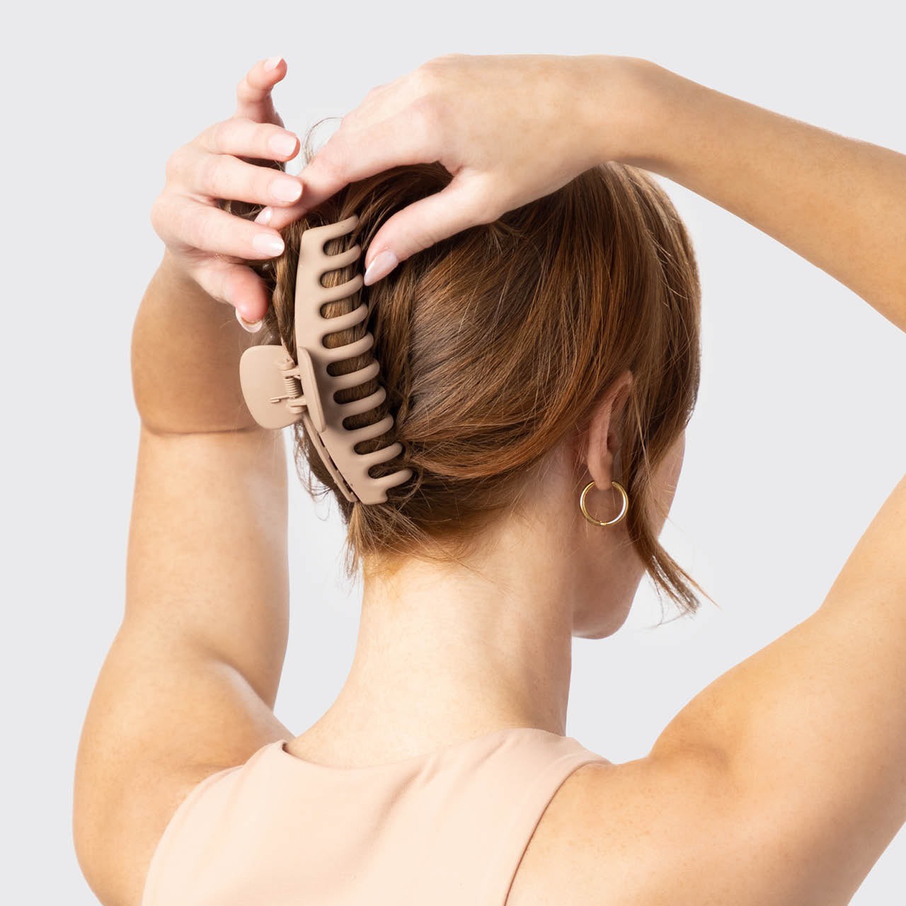 Person using a hair tool to style their hair against a light background
