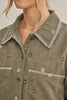 Close-up of a person wearing an olive green corduroy button-up shirt with white embroidered floral details and contrast stitching on the collar and chest pockets.