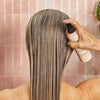Person applying a hair product to their wet hair with a pink tiled background