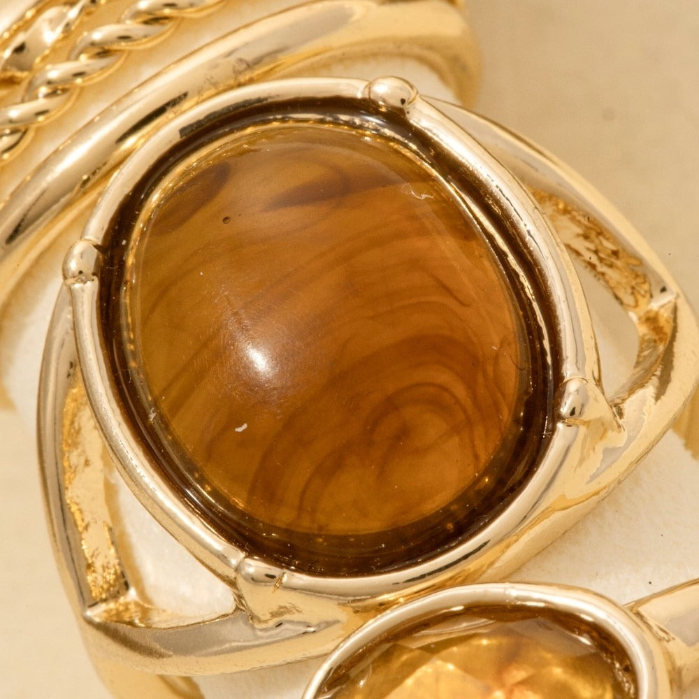 Gold ring featuring a large oval cabochon gemstone with a warm amber-brown marbled pattern, set in a polished yellow gold bezel.
