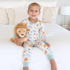 Child wearing a pajama set with animal prints, sitting on a bed holding a plush lion toy.