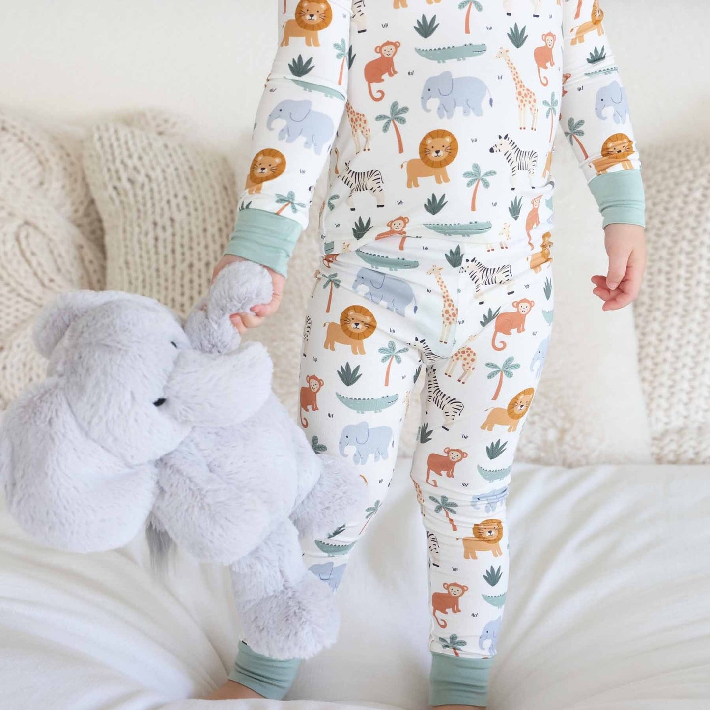 Child wearing pajamas with animal patterns holding a plush toy on a couch.