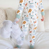 Child wearing pajamas with animal patterns holding a plush toy on a couch.