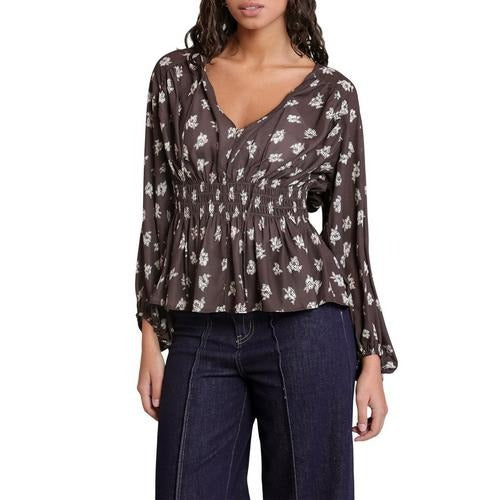 A woman wearing a dark brown long-sleeve blouse with a white floral pattern and dark blue jeans, shown against a plain white background.