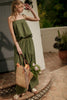 Woman in a green dress holding a woven bag with flowers on a stone step.