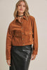 A woman wearing a cropped brown corduroy jacket with button details and flap pockets, paired with a black faux-leather skirt, against a plain beige background.