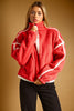 A woman wearing a red sherpa fleece zip-up jacket with white contrast stitching and white piping details, paired with black pants, set against a solid warm brown studio background.