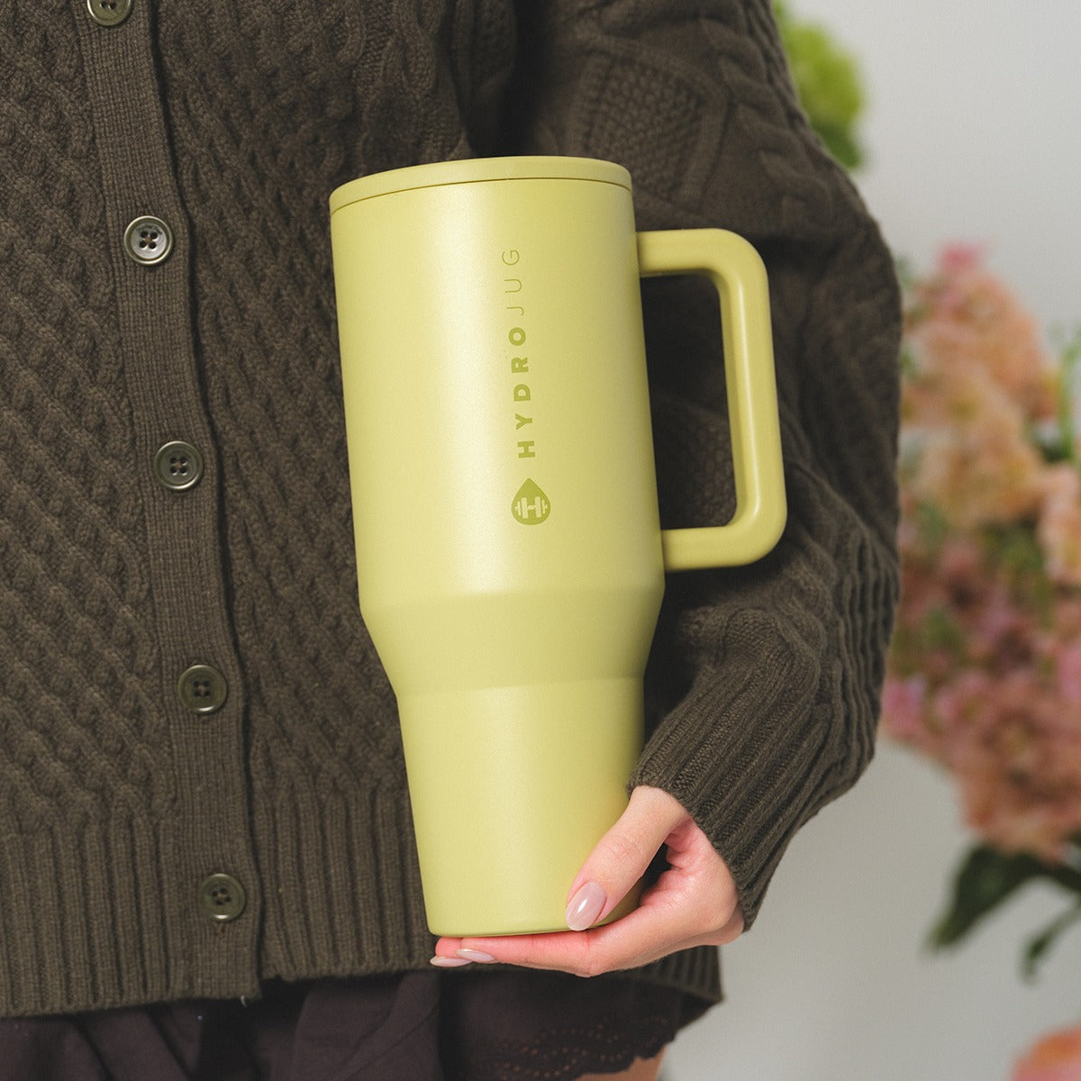 Person holding a yellow travel mug with 'Hydro Flask' branding, wearing a brown sweater.