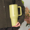 Person holding a yellow travel mug with 'Hydro Flask' branding, wearing a brown sweater.