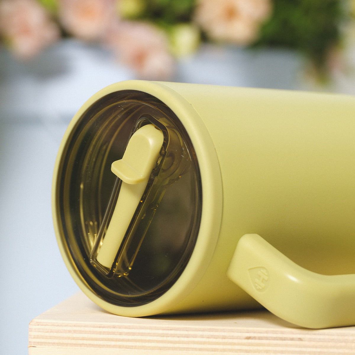 Yellow travel mug with a spoon on a wooden surface
