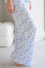 White maxi pajama pants with a blue bow and floral print, shown on a model standing barefoot on a light wood floor.