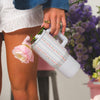 Person holding a floral-patterned thermos with pink flowers, blurred floral background