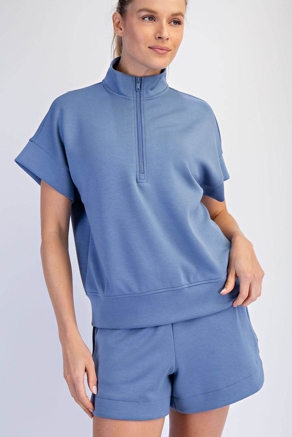 Woman wearing a blue outfit with a quarter-zip top and shorts on a white background