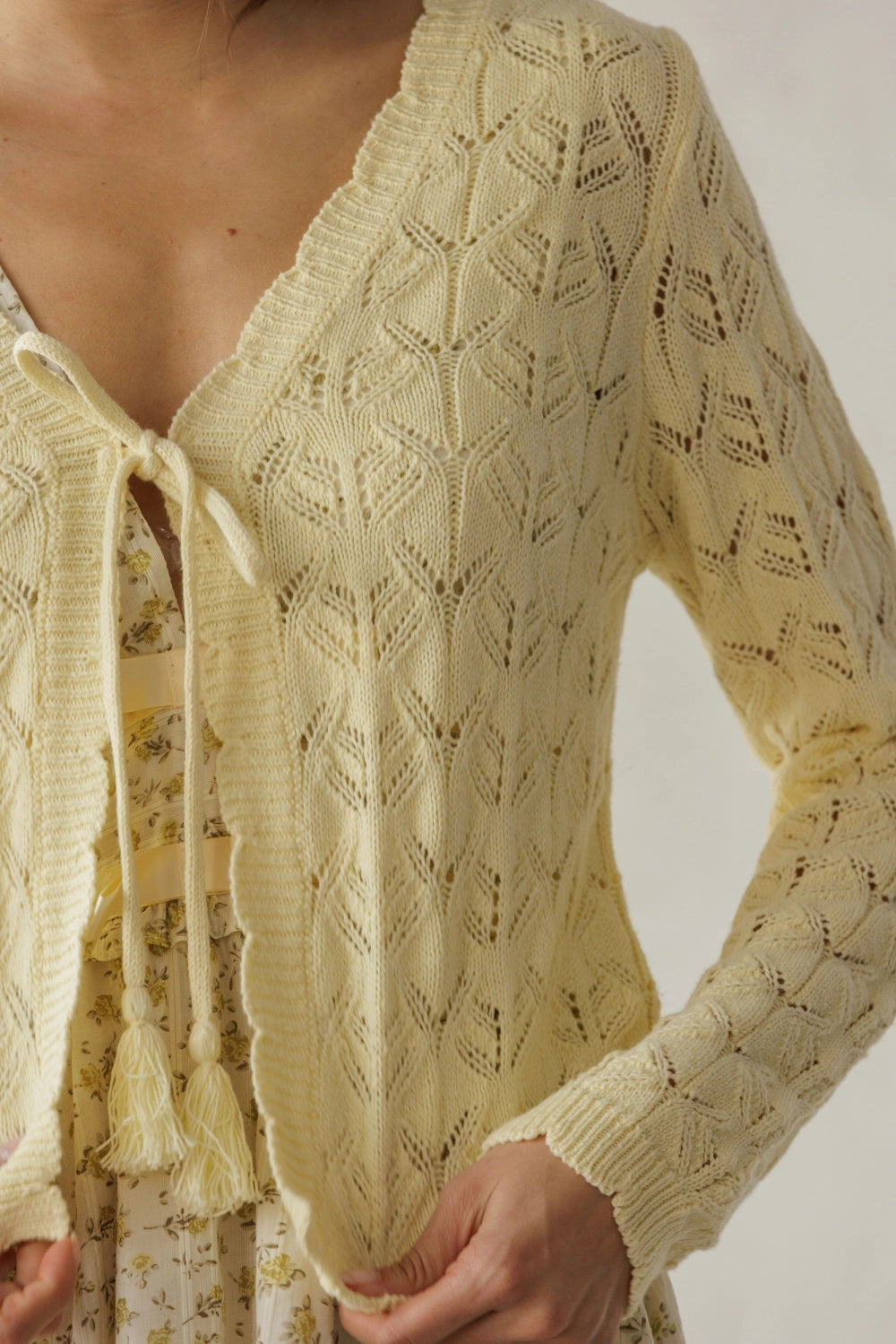 Close-up of a person wearing a light yellow lace cardigan with tassels.