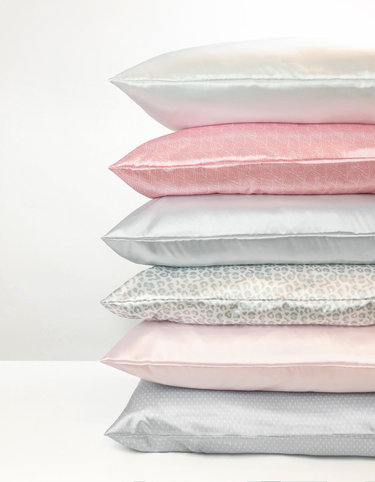 Stack of satin pillowcases in various colors on a white background