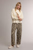 A woman modeling a cream-colored knit sweater with a giraffe graphic and matching leopard-print pants, standing against a neutral light gray studio background.