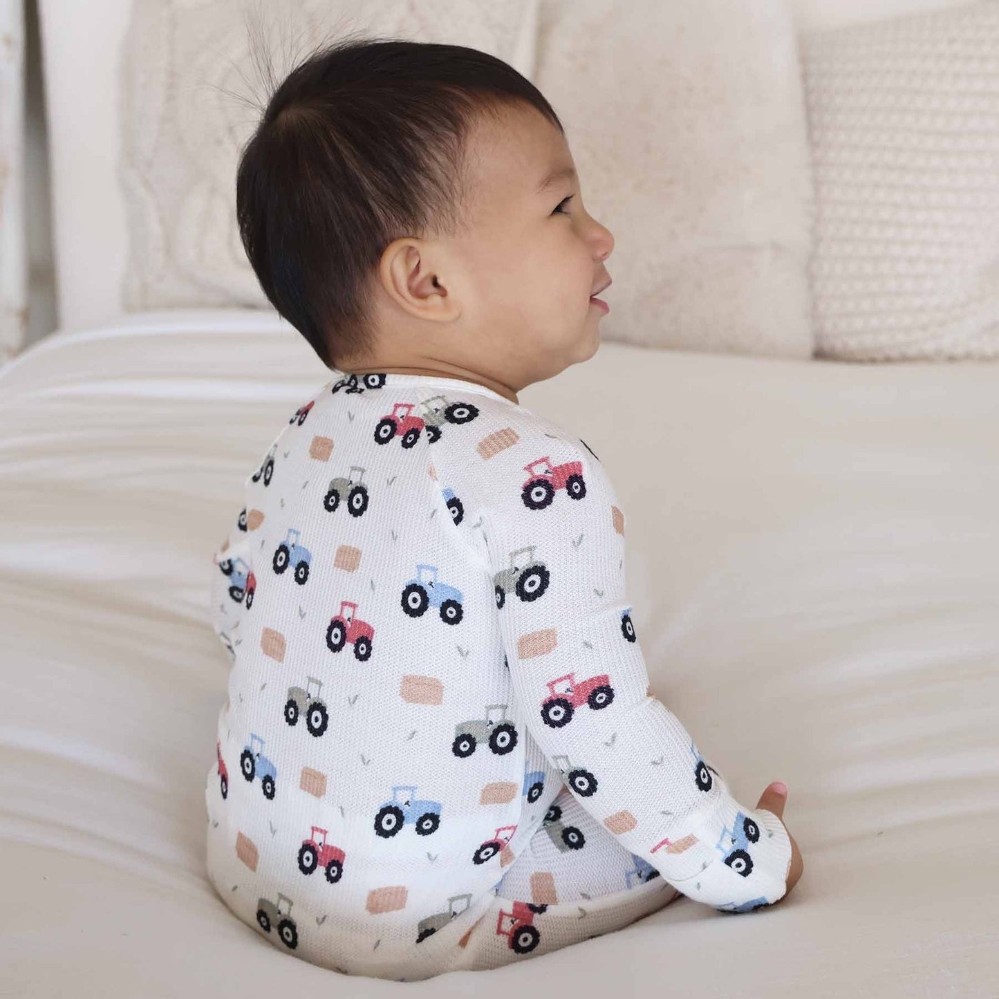 Child wearing a long-sleeve shirt with vehicle patterns sitting on a couch.