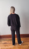 Person wearing a black outfit standing against a plain wall on a wooden floor.