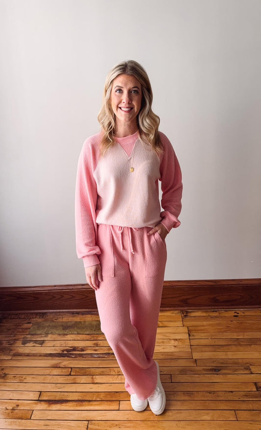 Woman wearing a pink outfit standing on a wooden floor with a white wall background
