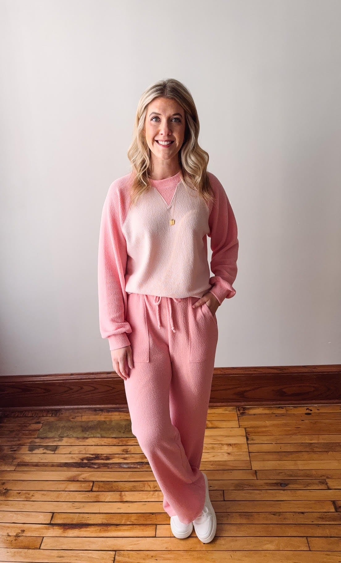 Woman wearing a pink outfit standing on a wooden floor with a white wall background