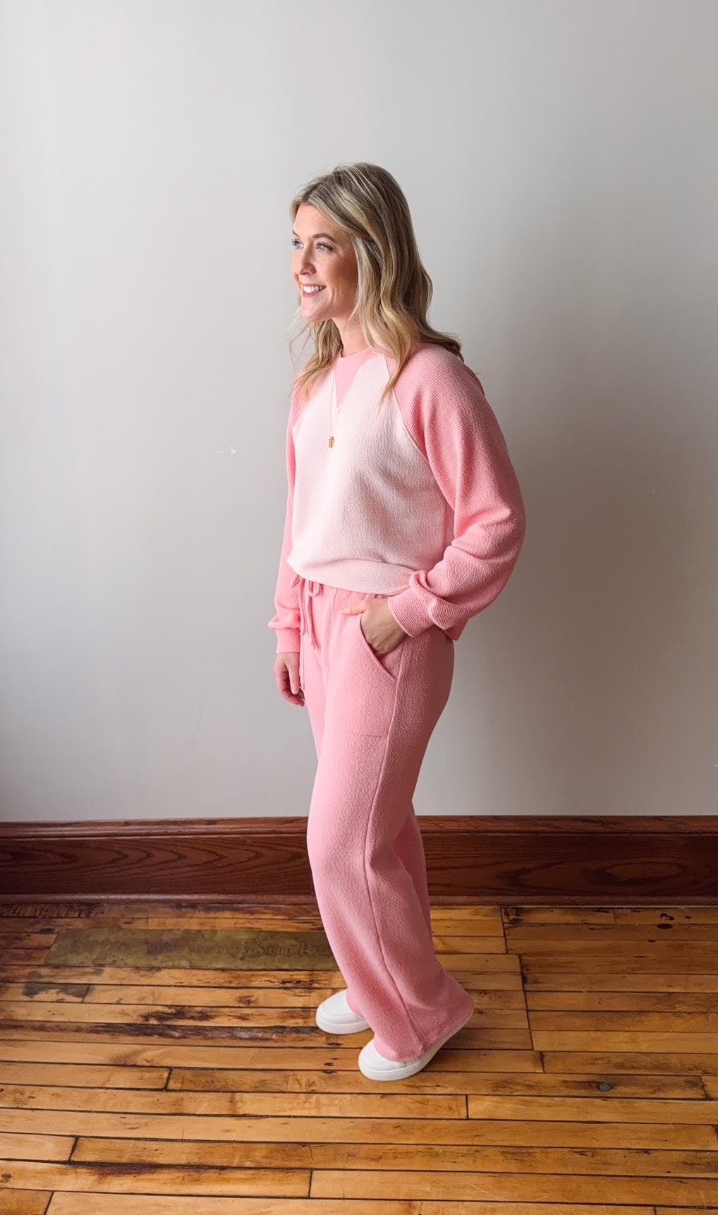 Woman wearing a pink tie-dye outfit standing on a wooden floor with a white wall background
