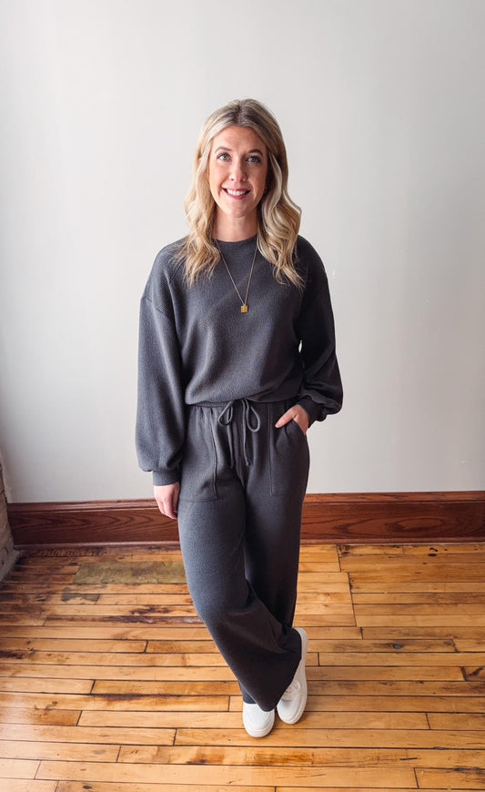Woman wearing a gray outfit standing on a wooden floor with a white wall background
