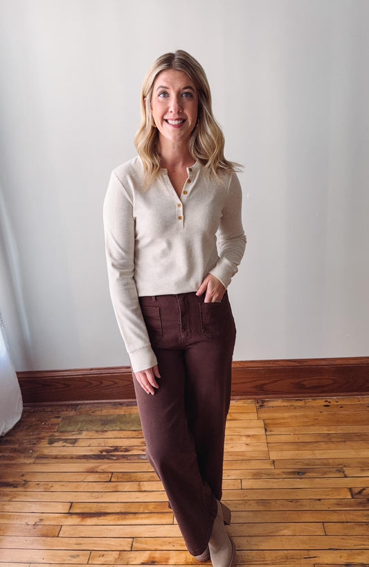 Woman wearing a cream sweater and brown pants standing on a wooden floor.