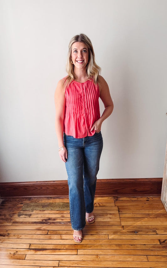 Woman wearing a pink top and blue jeans standing on a wooden floor against a white wall.