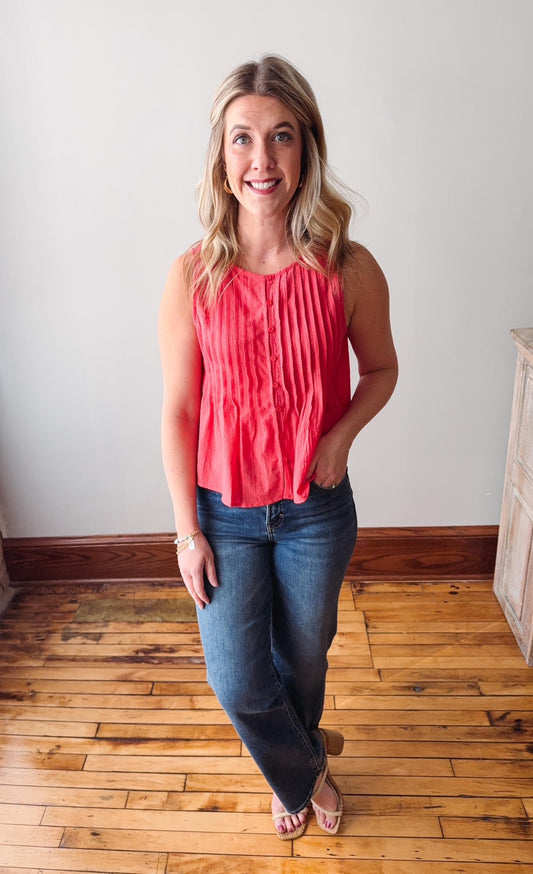 Woman wearing a coral top and blue jeans standing on a wooden floor.