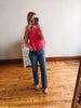 Woman taking a mirror selfie wearing a pink top and blue jeans in a room with wooden flooring.