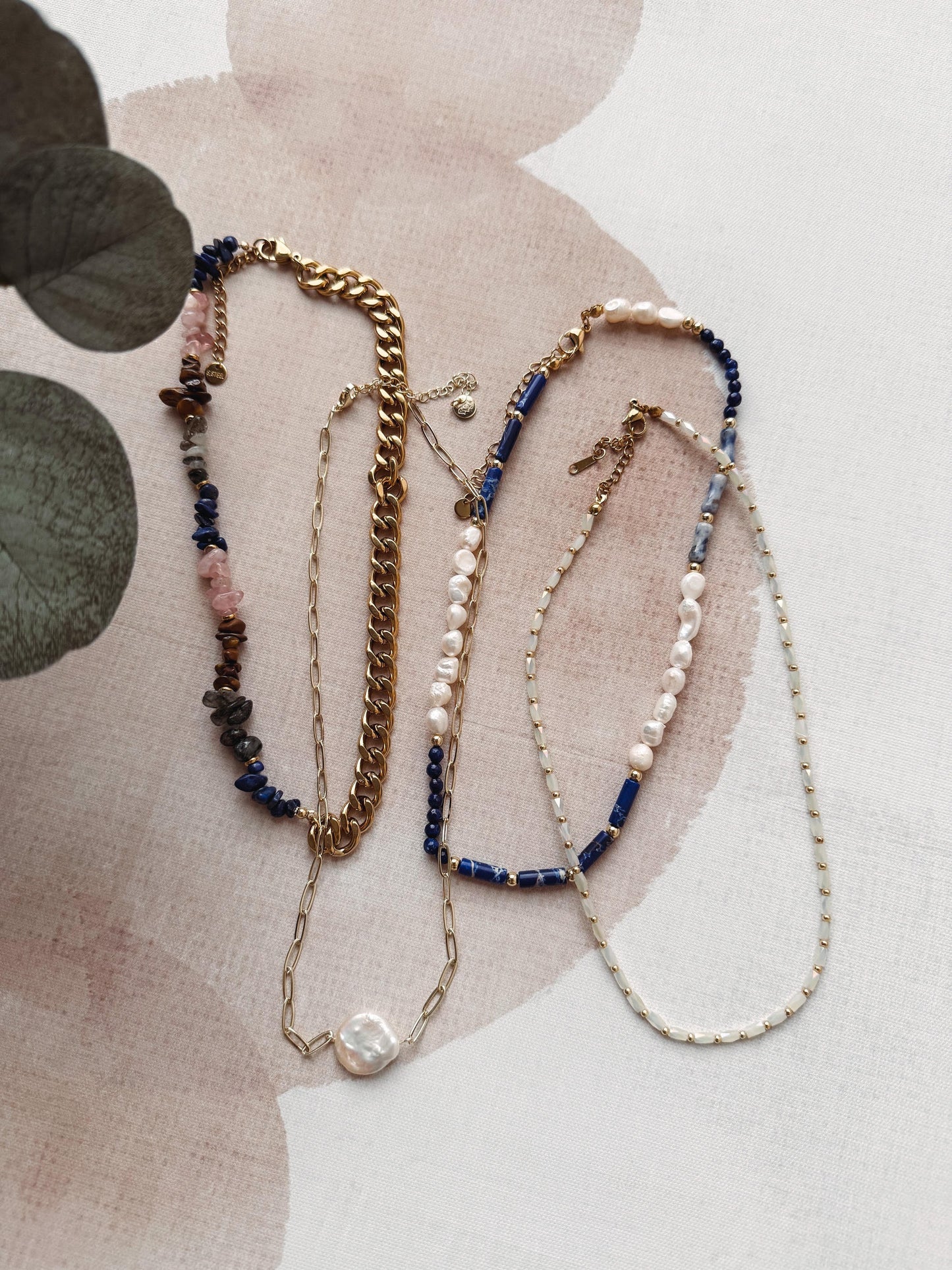 Three necklaces with beads and chains on a textured surface