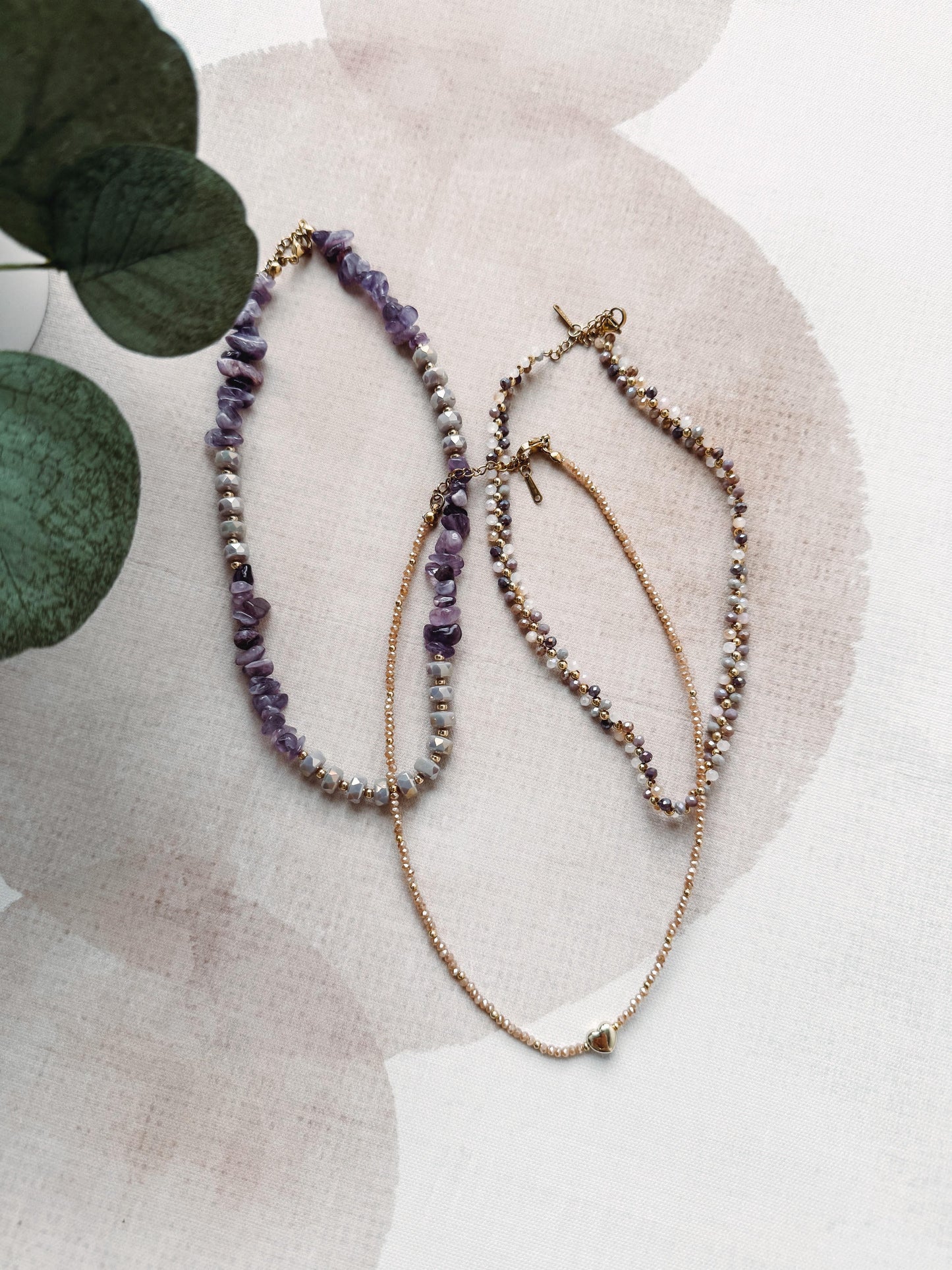 Three beaded necklaces on a textured surface with a plant in the background