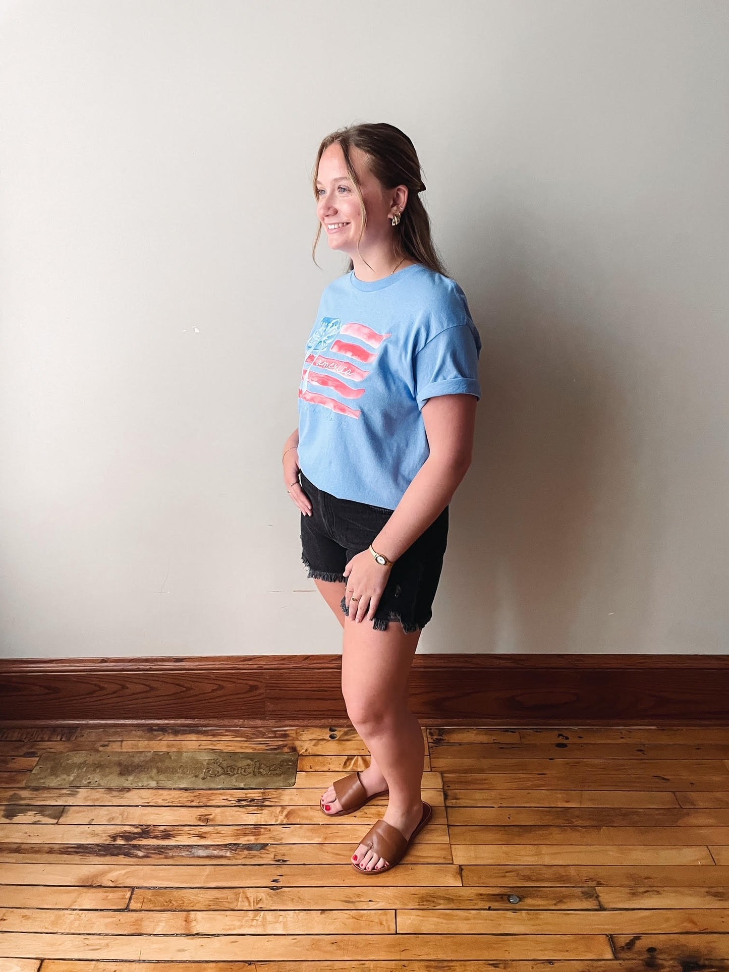Woman wearing a blue t-shirt with a graphic design on a wooden floor and white wall background