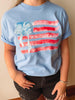Light blue t-shirt with American flag design and palm tree, worn by a person.