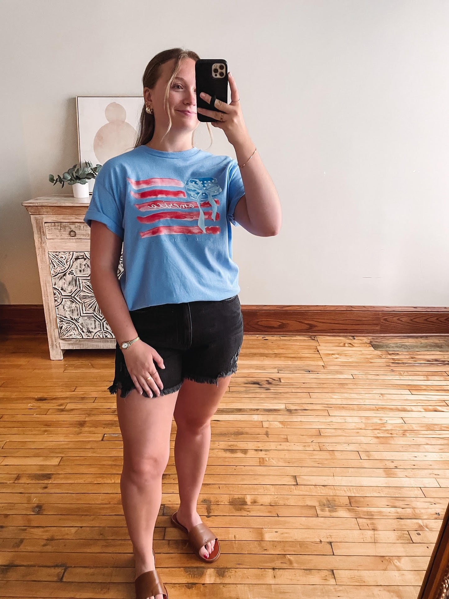 Person taking a mirror selfie wearing a blue t-shirt with an American flag design.