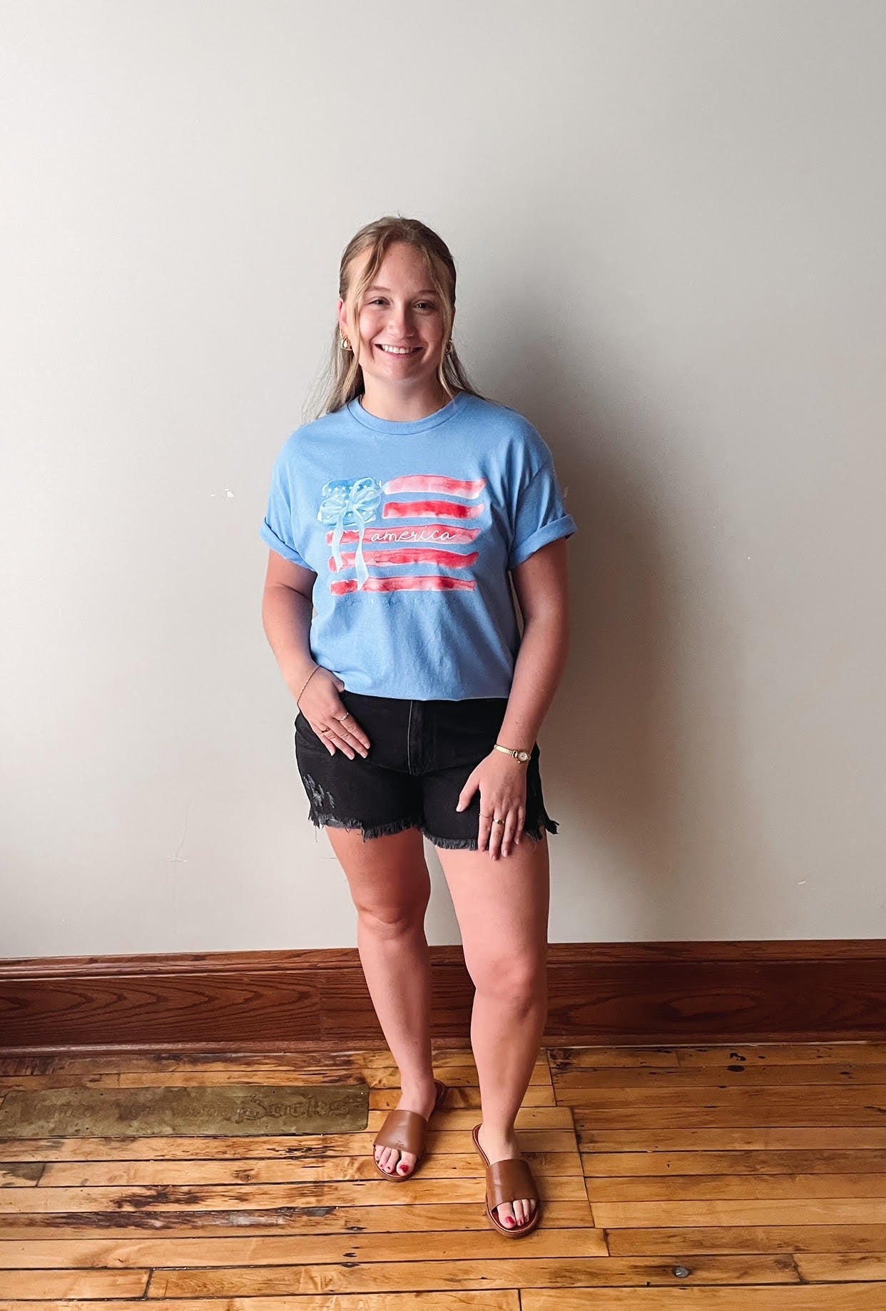 Woman wearing a blue t-shirt with an American flag design, standing against a plain wall.