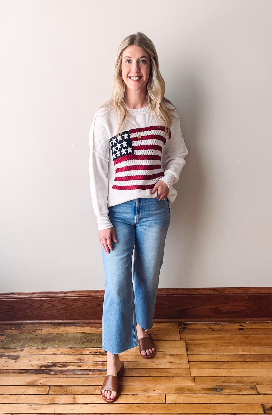 Woman wearing a sweater with a flag design standing against a plain background.