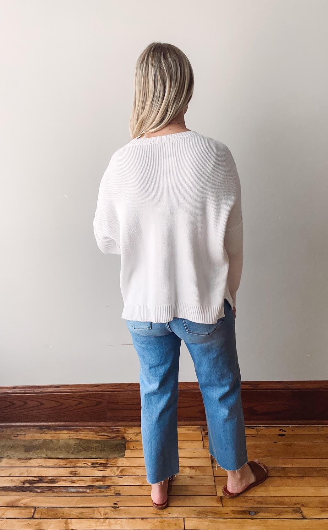 Person wearing a white sweater and blue jeans standing indoors.