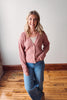 Woman wearing a pink cardigan and blue jeans standing on a wooden floor.
