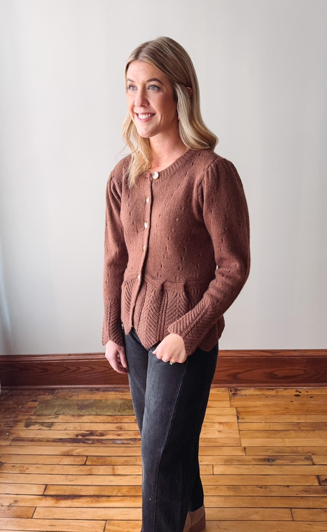Woman wearing a brown knitted cardigan standing on a wooden floor.
