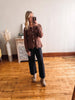 Woman taking a mirror selfie wearing a brown sweater and black pants in a room with wooden flooring.