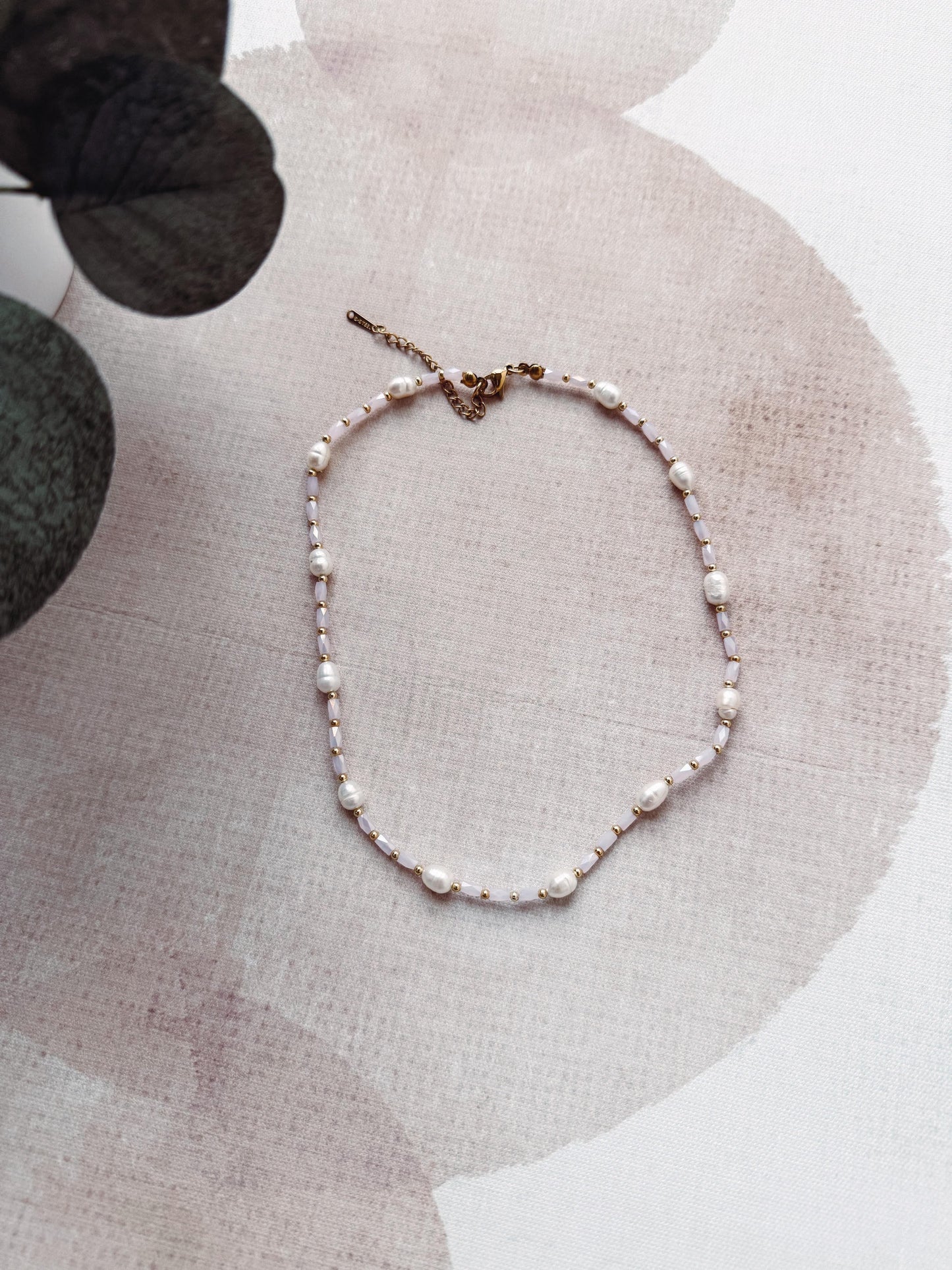 Pearl necklace on a textured surface with a plant in the background