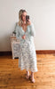 Woman taking a mirror selfie wearing a floral dress and gray cardigan in a room with wooden flooring.