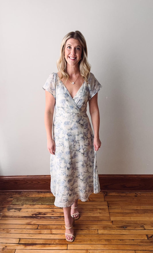 Woman wearing a floral dress standing on a wooden floor with a white wall background